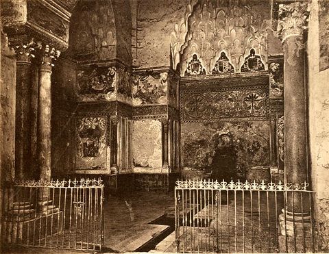 Sepia-toned photograph. From close to one of two pairs of framing columns, we look into a space with an arched alcove to our left and a honeycomb vault over a fountain to our right. The walls are frescoed, tiled, and mosaic, but details are difficult to make out because this photograph is rather dark.