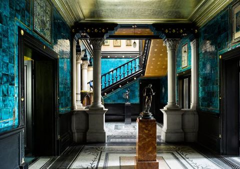 Architecture. An interior space has mosaic floors, aquamarine-blue tiled walls, and a gold ceiling. Stone columns separate this from a space beyond, which has staircase with a black wood railing.