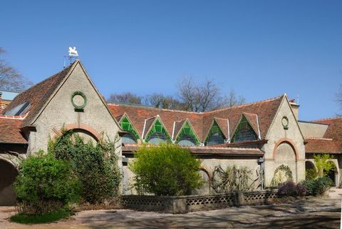 Architecture. This building has a series of gabled windows stretching between two peaked bays. The roof is terracotta brown and the face of the structure tan. In each gable, the space between the arched window below and a triangular peak above is filled with emerald-green tiles.