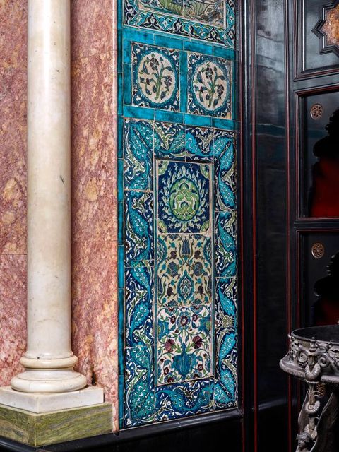 Architecture. Next to a white column, a tiled panel is patterned in mostly blue and white leafy designs, with touches of dark red and pale green.