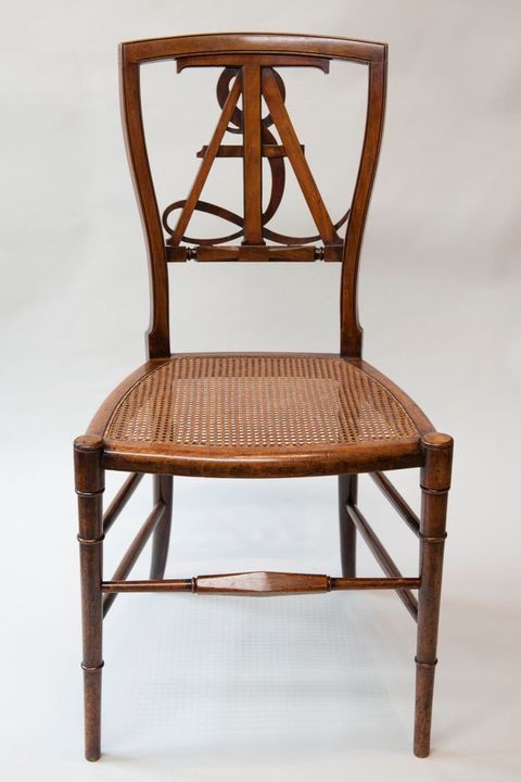 Watercolour. An arched opening in a wall painted deep gold has a dividing curtain in shades of pale red, pink and orange. The curtain is pulled back to reveal a richly decorated room beyond with ornate furniture, art objects and lavish soft furnishings. The walls and ceiling of the room are covered with patterns and ornamentation, and the polished black floorboards gleam.