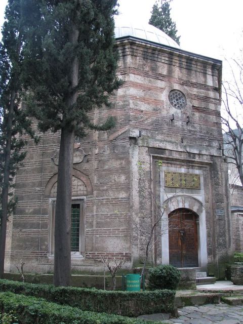 Architecture. The walls of an octagonal structure have horizontal brick courses separated by bands of stone. An arched double door is at the front, and a dome rises above.